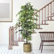 An artificial ficus tree in a basket with handles on a wooden floor.