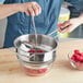 A person using a Choice Prep stainless steel rotary food mill to press raspberries into a metal bowl.