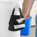 A person using a Lavex black double pocket trash bag dispenser to put a bag in a trash can.