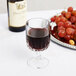 A Libbey Winchester wine glass filled with red wine on a table next to a plate of grapes.