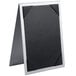 A black and silver Menu Solutions Alumitique table tent with picture corners holding a black and white menu on a table.
