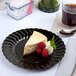 A slice of cheesecake with raspberries on a Fineline Flairware black plastic plate.