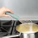 A hand with a grey and green handle using a Vollrath stainless steel whisk in a pot of liquid.