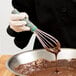 A person using a Vollrath stainless steel French whip to mix chocolate batter.