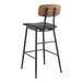 A Lancaster Table & Seating black metal barstool with a black vinyl seat and wood backrest.