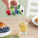 A hand pouring Ocean Spray Apple Juice into a glass on a table with a bowl of blueberries and a pastry.