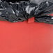 A black plastic bag in a red Continental 3200RD Huskee round trash can.