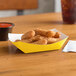 A yellow paper food tray filled with fried food next to a cup of sauce.