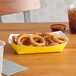 A yellow paper food tray with fried onion rings on a table.