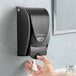 A person using a black SC Johnson Professional Proline Curve hand soap dispenser.