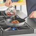 A person pouring sauce into a Vollrath Wear-Ever non-stick fry pan on a stove.