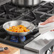 A person using a Vollrath Tribute stainless steel frying pan to cook food on a stove top.