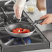 A person using a Vollrath Wear-Ever non-stick fry pan to cook food on a stove.