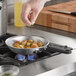 A hand cooks potatoes in a Vollrath Wear-Ever aluminum fry pan on a stove.