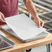 A person holding a sheet of 12" x 16" parchment paper over a tray.
