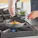 A person in gloves cooking food in a Vollrath Wear-Ever aluminum non-stick fry pan.