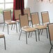 A group of Lancaster Table & Seating banquet chairs with tan vinyl and black frames in a room.