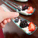 A person's hand holding a Fineline Tiny Temptations green plastic spoon with fruit in it.