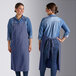 Two women wearing Acopa Ashville Ocean Linen adjustable bib aprons over jeans at a professional kitchen counter.