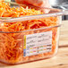 A person using a Carlisle clear polycarbonate food pan to store shredded carrots on a salad bar counter.