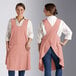 Two women wearing Acopa Ashville mauve linen smock bib aprons with pockets.