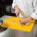 A person cutting chicken on a yellow Tablecraft flexible cutting board.