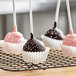 White fluted mini baking cups on a cooling rack with chocolate covered cake pops.