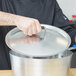 A chef using a Vollrath aluminum lid with a white Torogard handle.