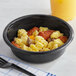 A black bowl filled with scrambled eggs, sausage, and cheese.