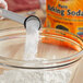 A person using a white scoop to pour Arm & Hammer Baking Soda into a bowl.