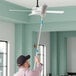 A man using a Lavex 15" Duster Brush to clean a ceiling fan.