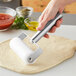 A hand using a Choice dough roller with stainless steel handles to roll out pizza dough.