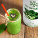 A green smoothie in a jar with a straw next to a Smartfruit Harvest Greens Puree bottle.