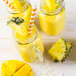 A glass jar filled with yellow Smartfruit Aloha Pineapple puree with a straw and a pineapple wedge.