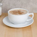 A white CAC Clinton cappuccino cup on a saucer with brown foam in it.