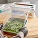 A person in gloves using a serrated cutter to cut Berry standard plastic film over a tray of spinach.