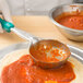 A person uses a Vollrath teal spoodle to scoop red sauce into a bowl.