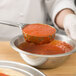 A hand using a Vollrath teal Spoodle to scoop red sauce into a bowl.