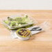 A Genpak clear plastic deli container with salad and lettuce, and a fork on a table.