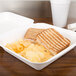 A white Bare by Solo sugarcane take-out container with a sandwich and chips.
