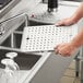 A person holding a Regency stainless steel sink cover with holes over a sink.