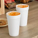 Two white Dart styrofoam cups with ice tea on a table.
