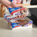 A hand holding a package of Hostess Glazed Blueberry Donettes in front of a cash register.
