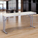A National Public Seating speckled gray plastic folding seminar table on a wood floor.