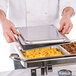 A person holding a Carlisle stainless steel hinged tray cover over a tray of food.