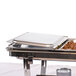 A Carlisle stainless steel hinged cover on a metal tray with food inside.