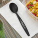 A black Stalk Market CPLA spoon on a napkin next to a bowl of corn.