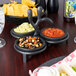 A black HS Inc. salsa caddy holding three bowls of salsa on a table with food and drinks.