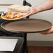A hand holding a Carlisle brown non skid fiberglass serving tray with a sandwich with ham and cheese on it.