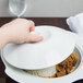 A hand holding a CAC porcelain lid over a white plate of food.